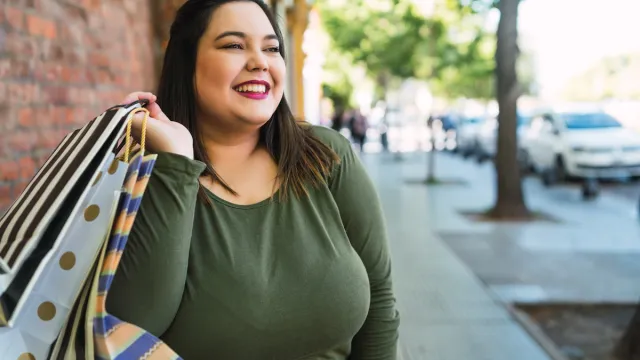 Portrait of young plus size woman holding shopping bags outdoors on the street.