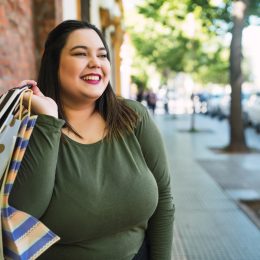 Portrait of young plus size woman holding shopping bags outdoors on the street.
