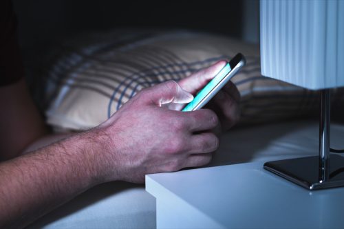 close-up of man's using his smartphone in bed at night