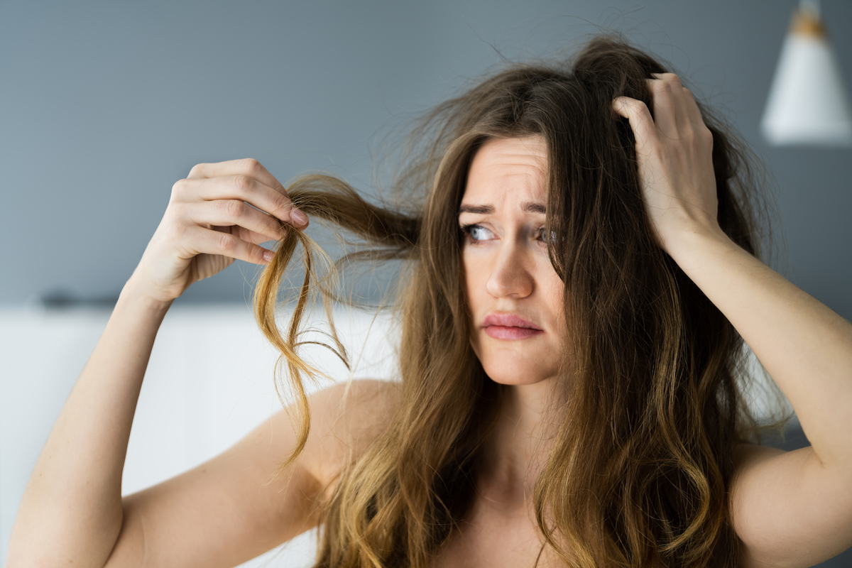 Upset woman with long, wavy brown hair looking at her damaged hair