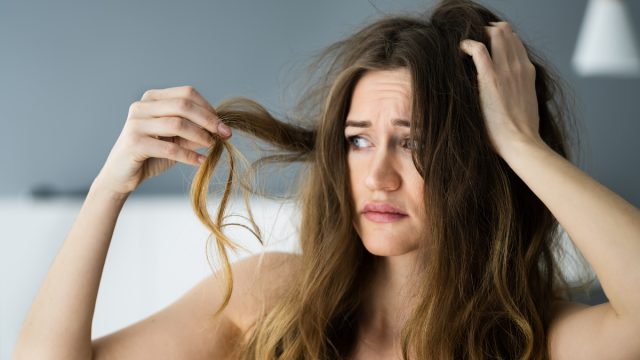 Upset woman with long, wavy brown hair looking at her damaged hair