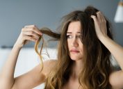 Upset woman with long, wavy brown hair looking at her damaged hair
