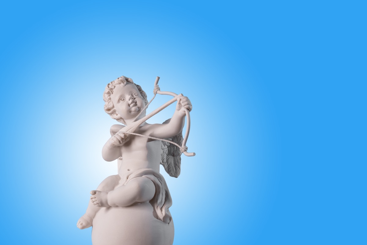 Figurine of an angel Cupid on the podium with a bow and arrow on a blu background