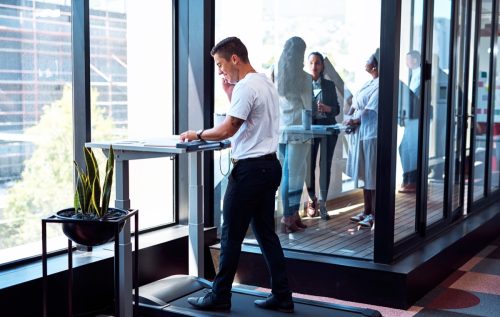 Shot of a young businessman talking on a cellphone and going through paperwork while walking on a treadmill in an office