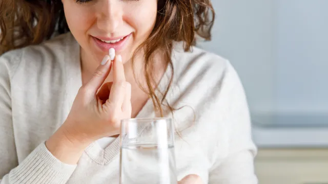 Smiling young woman taking medication at home with glass of water
