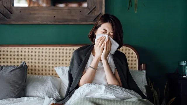 A young woman sitting in bed while blowing her nose