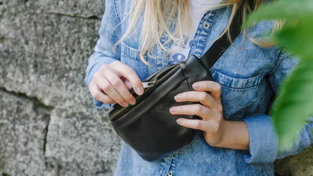 Blonde girl in a blue denim shirt is wearing a black leather belt bag across her chest.