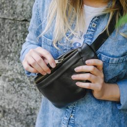 Blonde girl in a blue denim shirt is wearing a black leather belt bag across her chest.