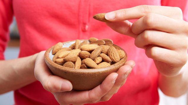 Cropped image of a woman wearing a coral-colored sweater holding a small bowl of almonds