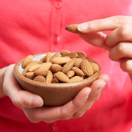 Cropped image of a woman wearing a coral-colored sweater holding a small bowl of almonds