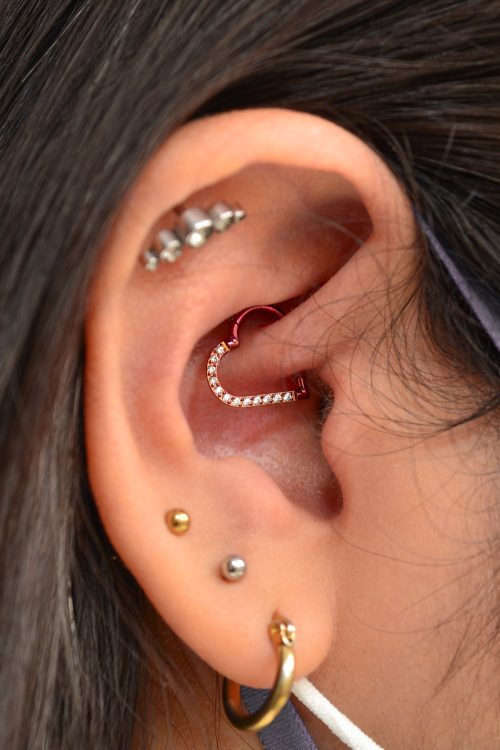 Close up of a woman's ear with a daith piercing, lobe piercing, and cartilage piercing.
