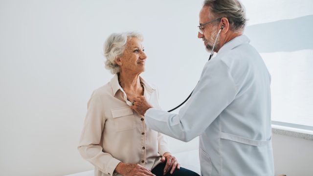 Doctor listening to senior woman patient heartbeat