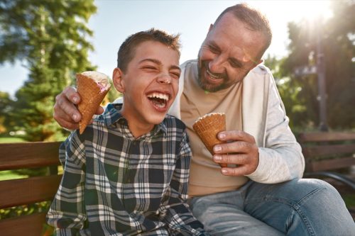 father and son laughing on a park bench while eating ice cream