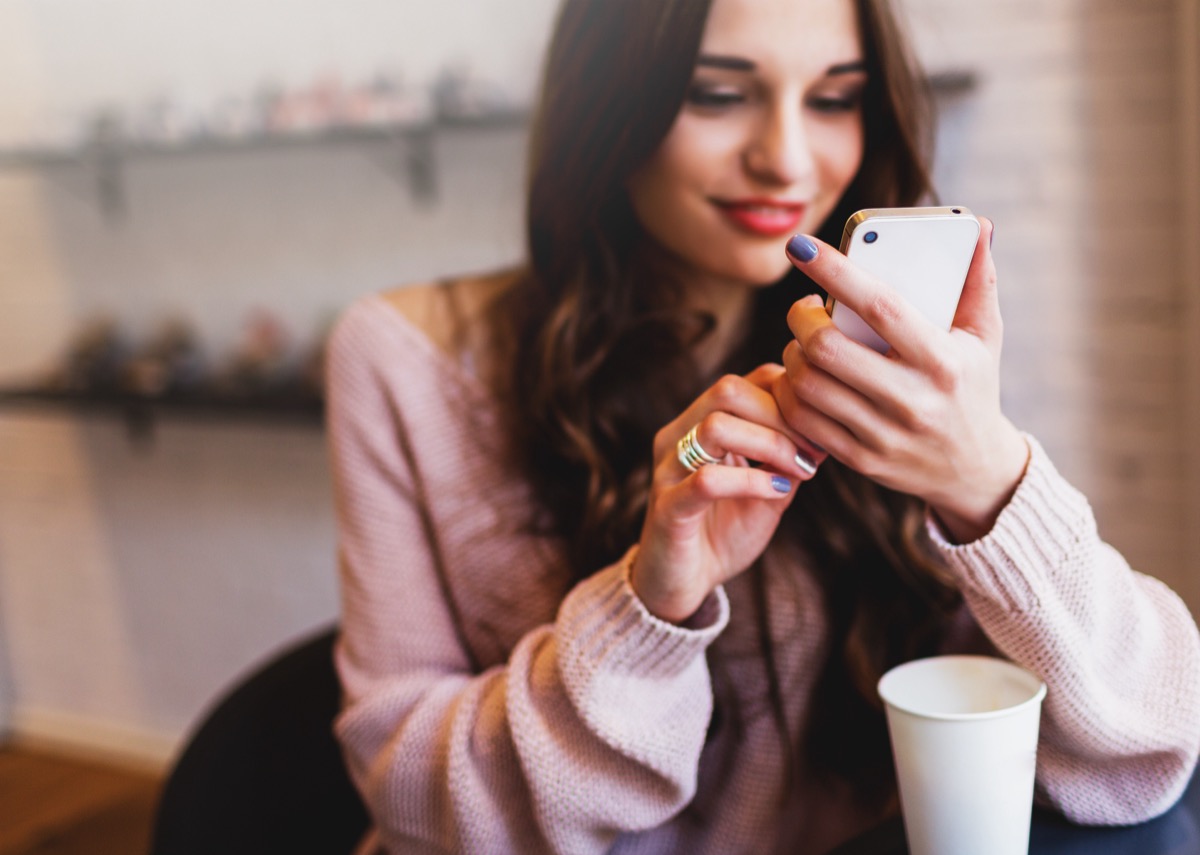 Attractive Woman wearing a pink blouse Texting while sitting at a coffee shop