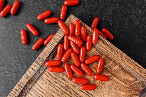 Red coenzyme q10 supplement softgels on chalkboard background and on wooden board.