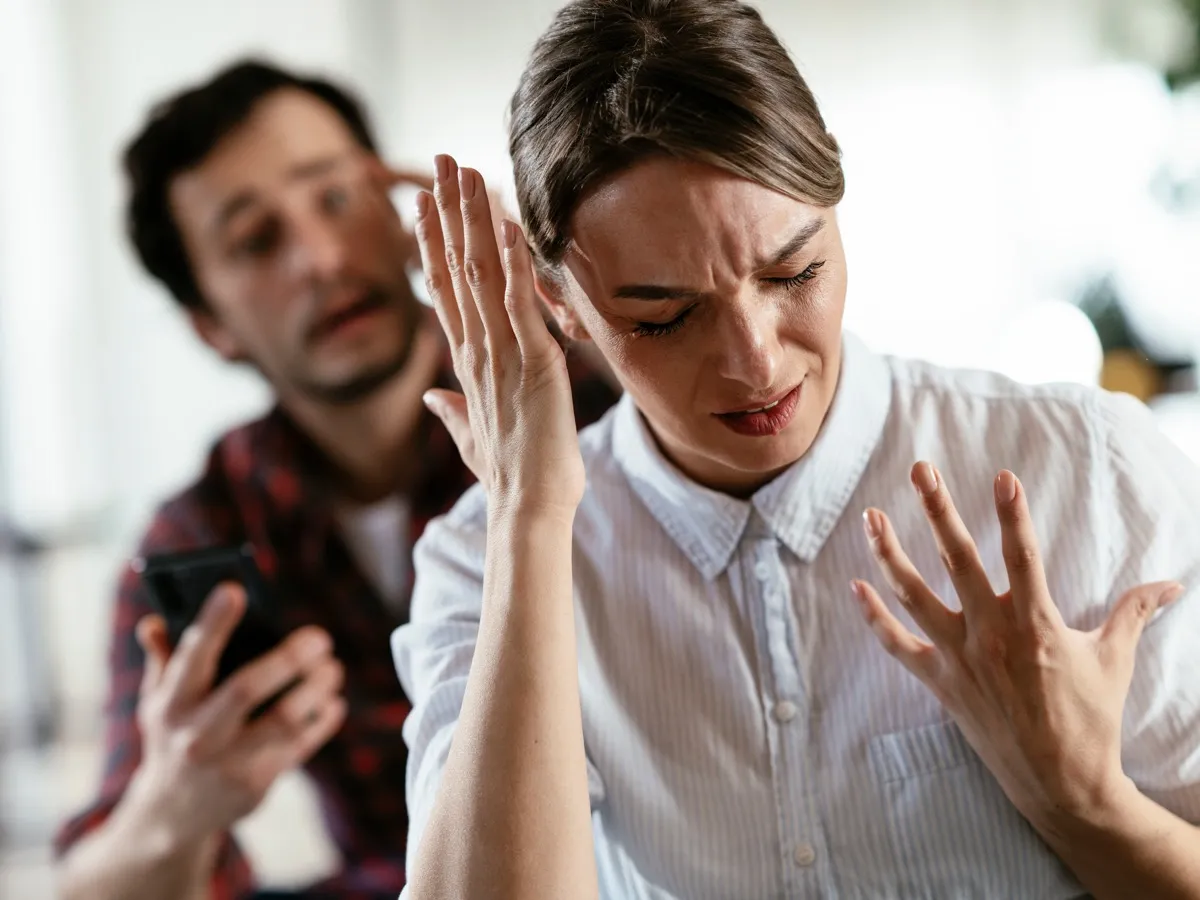 Couple Having a Fight; man is yelling in background with woman putting her hands up in frustration in foreground