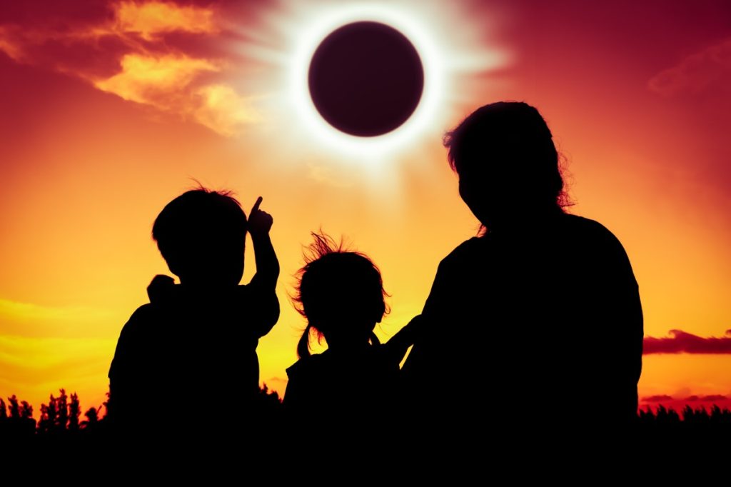 Silhouette of little boy, girl, and mother watching solar eclipse