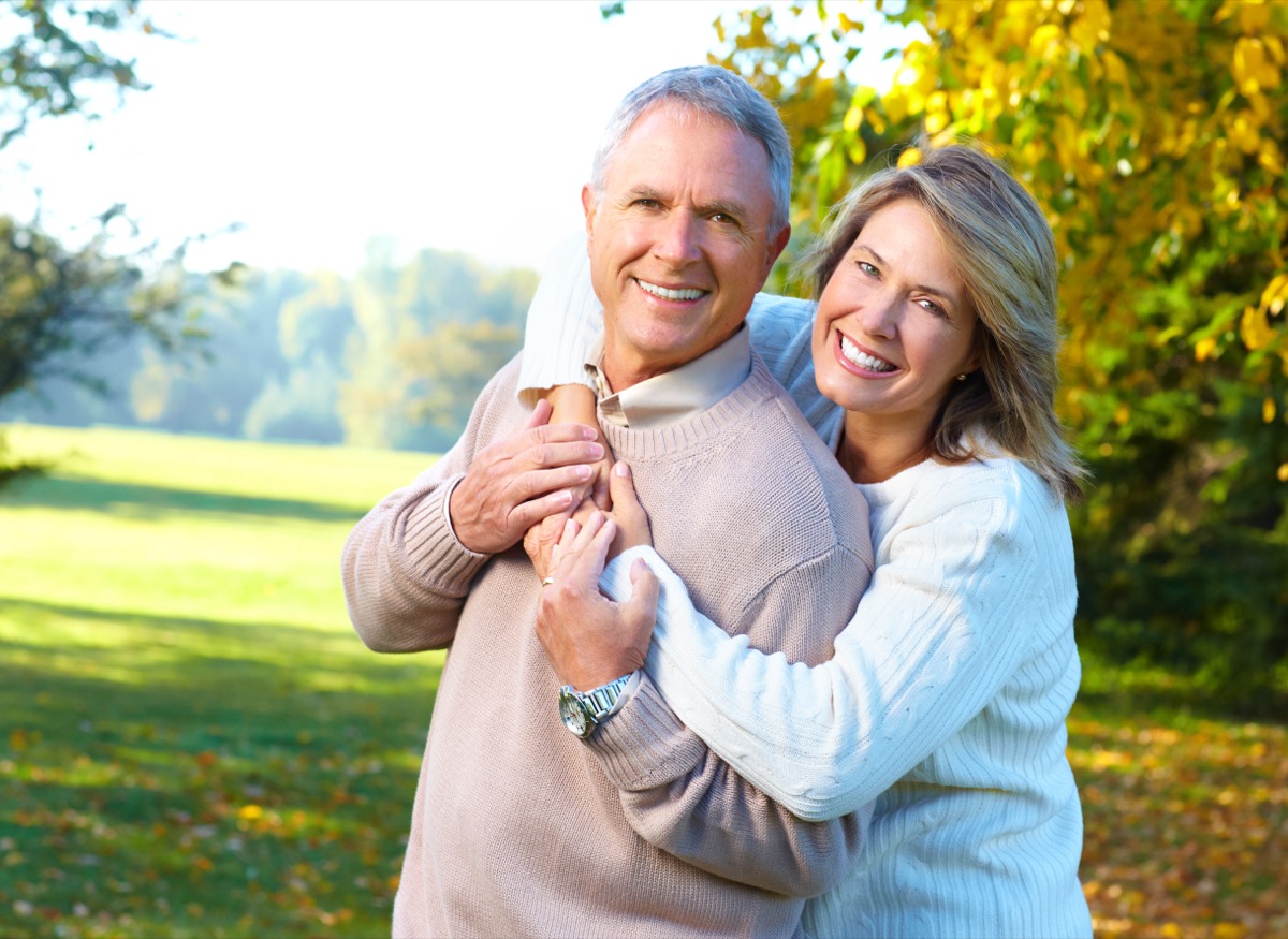A mature mana and woman hugging and smiling at the camera while in a park
