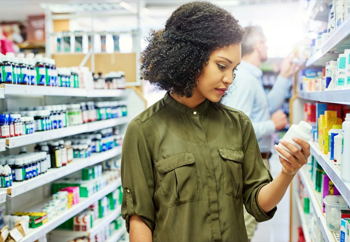 Pharmacy, health shop and woman with medicine for reading label, check product and choice in retail store. African female person looking at drugstore pills for ingredients, information and shopping