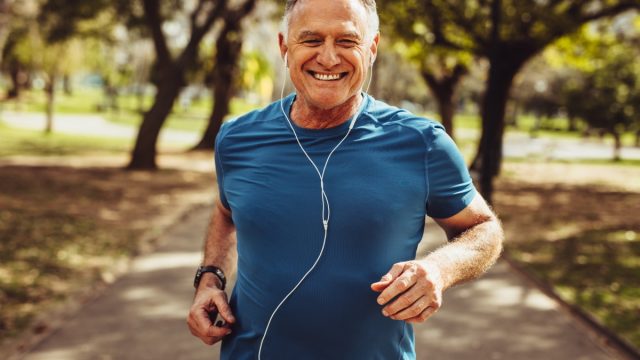 Portrait of a senior man in fitness wear running in a park. Close up of a smiling man running while listening to music using earphones.