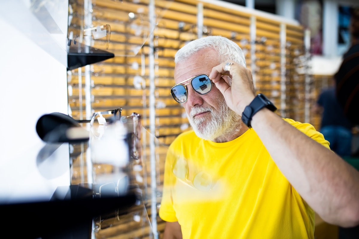 A senior man chooses sunglasses in an optical shop.