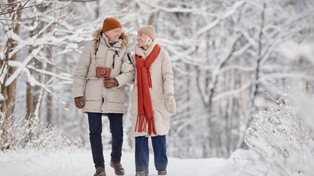 Full length portrait of happy senior couple enjoying walk in winter forest and looking at each other with love, copy space