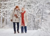 Full length portrait of happy senior couple enjoying walk in winter forest and looking at each other with love, copy space