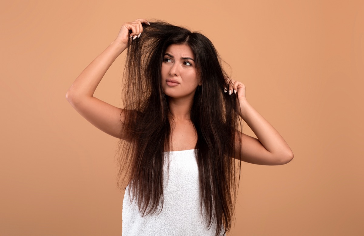 Frustrated armenian woman showing her damaged long locks on beige studio background. Young lady having bad hair day, upset over her messy hairdo. Hairdressing services concept