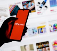 A smartphone with the AliExpress logo in a hand on background of the catalog from the site.