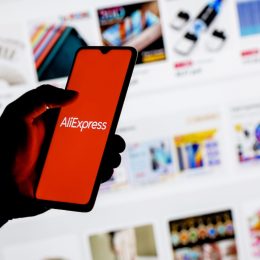 A smartphone with the AliExpress logo in a hand on background of the catalog from the site.