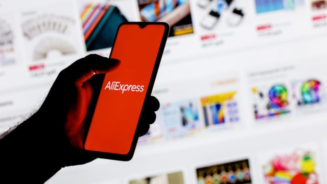 A smartphone with the AliExpress logo in a hand on background of the catalog from the site.