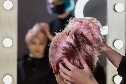 Back of a woman's had at a salon as stylist cuts her pink hair into a pixie cut