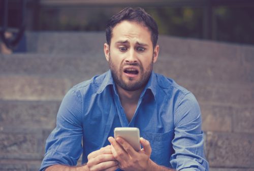 man looking upset while reading funny insults off his phone