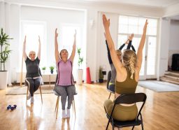 Female yoga instructor having yoga class with senior people on chairs in yoga studio
