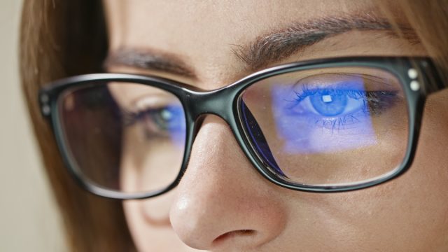 Close-up shot of woman eyes in glasses reflecting a working computer blue screen