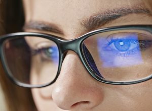 Close-up shot of woman eyes in glasses reflecting a working computer blue screen