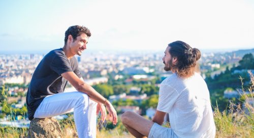 two men having a deep conversation while sitting on a hill overlooking the city
