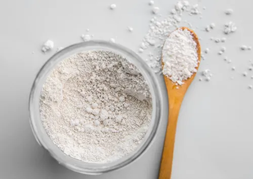 Diatomaceous earth also known as diatomite mixed in glass jar and wood spoon on gray background, studio shot.