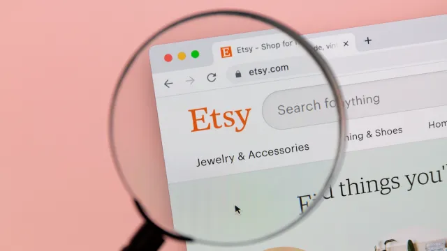 A magnifying lass over the Etsy logo on an internet page, against a light pink background
