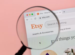 A magnifying lass over the Etsy logo on an internet page, against a light pink background