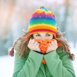 Portrait of a young woman in snow with scarf on her face trying to warm herself. Winter concept