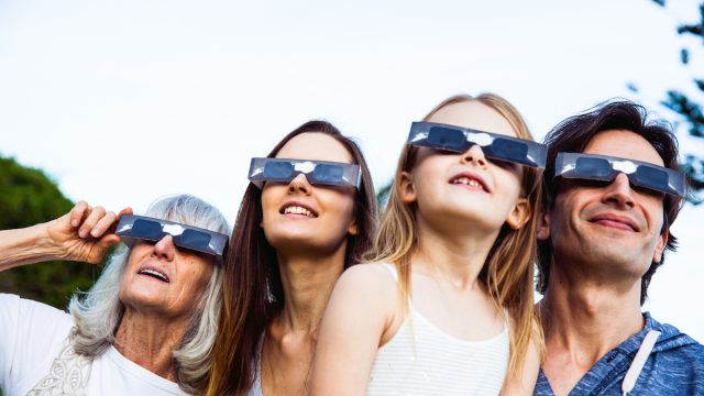 Family looking at Solar Eclipse using solar glasses. Parents with young daughter and grandmother.