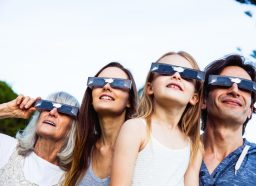Family looking at Solar Eclipse using solar glasses. Parents with young daughter and grandmother.