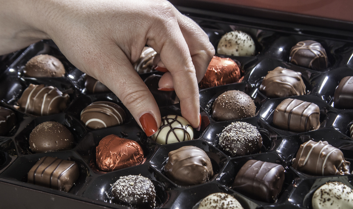 Female hand with red nail polish, taking a piece of white chocolate from a chocolate box