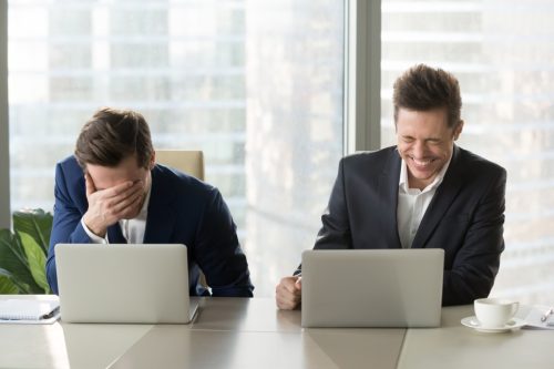 two male coworkers laughing together while working on their laptops