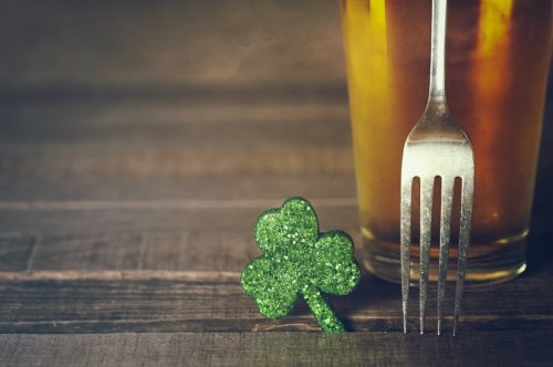 Closeup of St. Patricks Day green shamrock with fork and frosty cold glass of beer