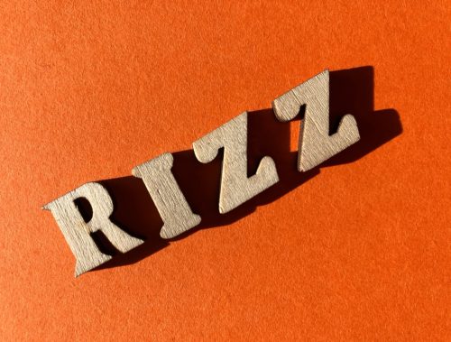 Rizz, slang word for charisma used by Gen Z, in wooded alphabet letters isolated on bright orange background