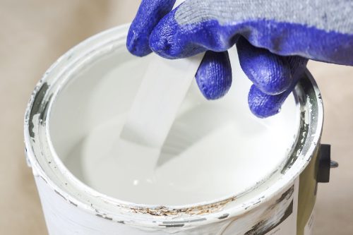 Hand wearing a purple work glove mixing a can of white paint