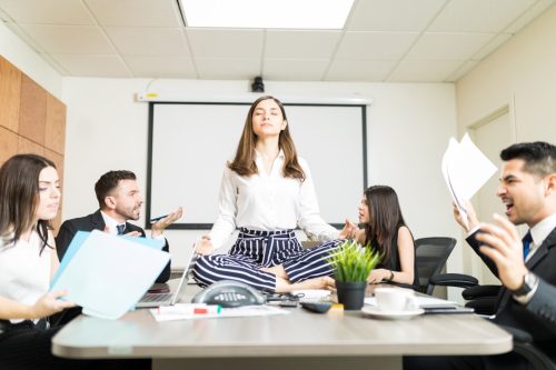 Young businesswoman meditating in lotus position while her colleagues yell during a negotiation in the office