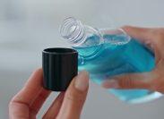 Woman hands pouring mouthwash in cap indoors close up. Unknown lady holding blue antibacterial liquid at bathroom. Unrecognizable girl using refreshing dental rinse. Morning care in bath room concept